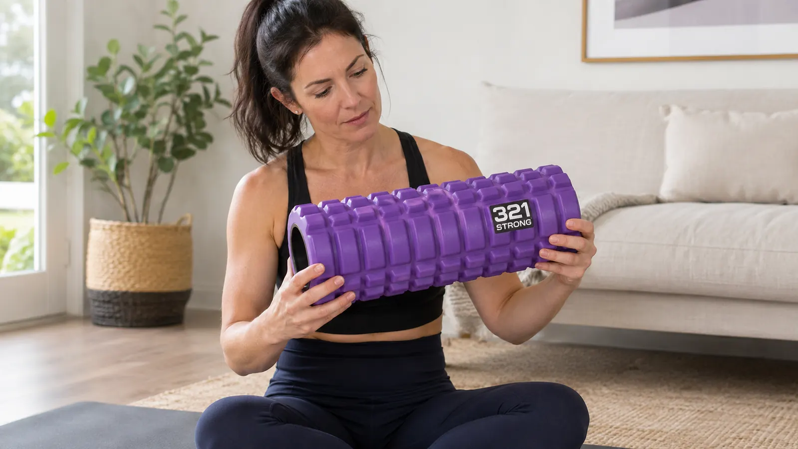 Woman using the 321 Strong foam roller on her calf while seated on a yoga mat