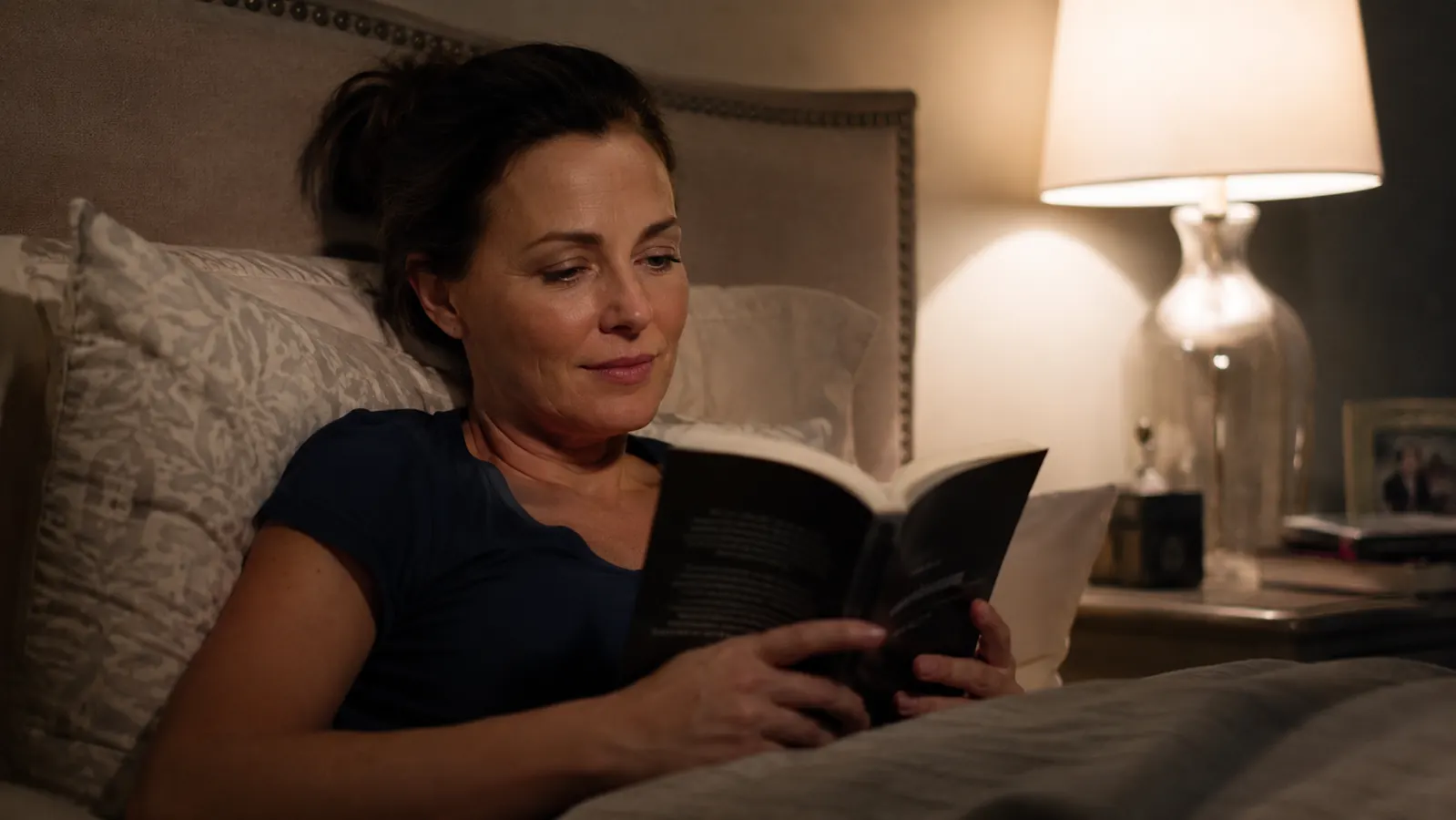 Tired woman sitting on the edge of a hotel bed at night, shoes on, still in work clothes, head resting in her hands