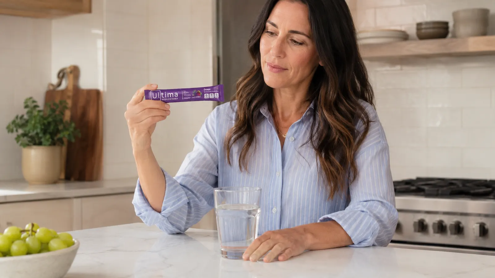 Hand tearing open an Ultima Replenisher stick pack over a stainless water bottle
